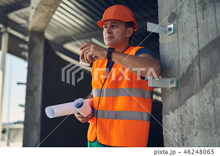 Confident foreman standing with his drawings and looking into the distance Confident foreman standing with his drawings and looking into the distance 46248065