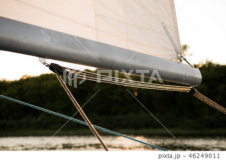 Close up on the boom mast of a sailing yacht, with sail and rigging ropes, and river or lake coast Close up on the boom mast of a sailing yacht, with sail and rigging ropes, and river or lake coast 46249011