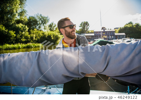 Young sailor in sunglasses holds and moves main sail with both hands. He is happy and smiling. Young Young sailor in sunglasses holds and moves main sail with both hands. He is happy and smiling. Young 46249122