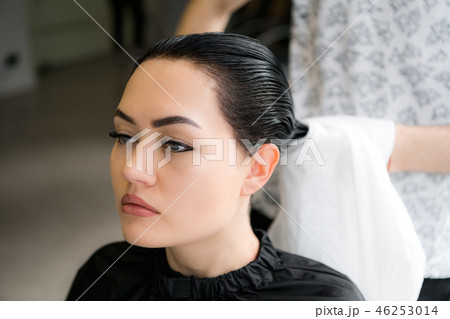 Charming young woman smiling happily while professional male hairstylist preparing her hair for the 46253014