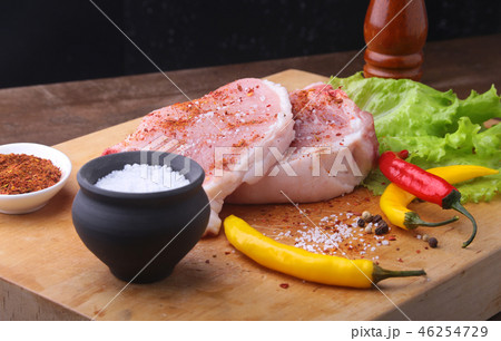 Raw steak, chop on a rustic cutting board with salt, pepper and grinder for spices . Black Raw steak, chop on a rustic cutting board with salt, pepper and grinder for spices . Black 46254729