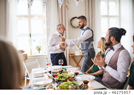 A man giving a bottle of wine to his father on indoor birthday party, a celebration concept. 46275957