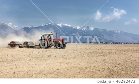 Tractor pulling heavy metal roller over dry field 46282472