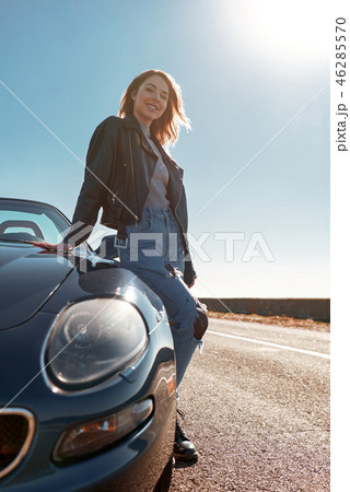 Young woman standing near roofless car in leather jacket Young woman standing near roofless car in leather jacket 46285570