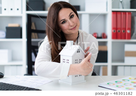 Young girl sitting at the table and holding hands near the layout of the house. 46301182