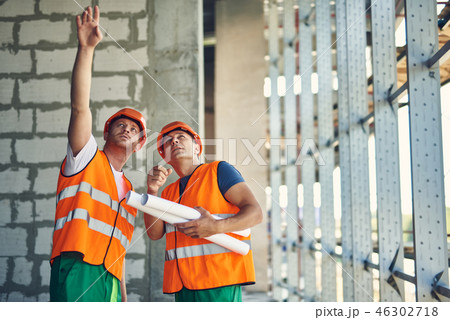Thoughtful builder pointing to the ceiling while standing with coworker 46302718