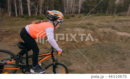 One caucasian children rides bike road track in dirt park. Girl riding black orange cycle in One caucasian children rides bike road track in dirt park. Girl riding black orange cycle in 46310670