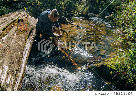 Beautiful girl drinking water from river on log after travel. Woman traveler in summer passes on 46311534
