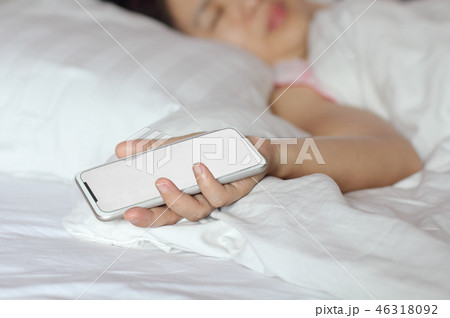 Woman sleeping in bed and holding a cell phone. 46318092