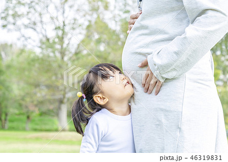 公園で妊娠しているお母さんの大きなお腹に顔を当て見上げる幼い女の子。親子、家族、愛、幸せ、妊娠イメー 46319831