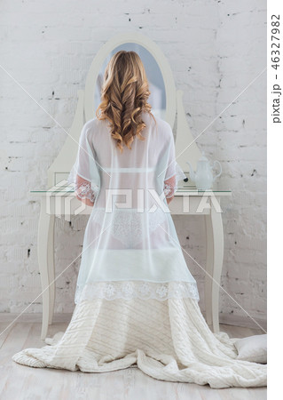 Gentle woman in white lingerie sits behind the night table 46327982