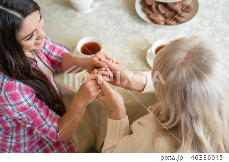 Elderly mother and her daughter holding hands while sitting at the table 46336045