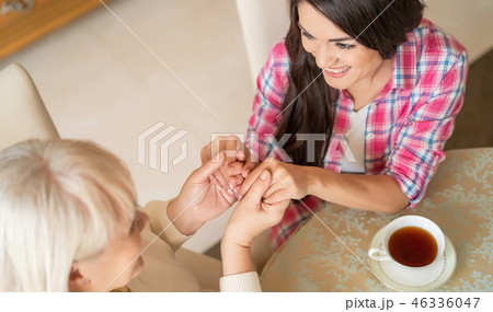 Elderly mother and her daughter holding hands while sitting at the table 46336047