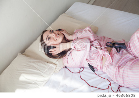 woman in pajamas on the bed listening to music headphones 46366808