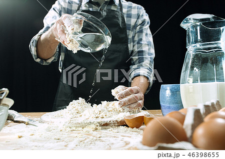 Professional male cook sprinkles dough with flour, preapares or bakes bread at kitchen table Professional male cook sprinkles dough with flour, preapares or bakes bread at kitchen table 46398655