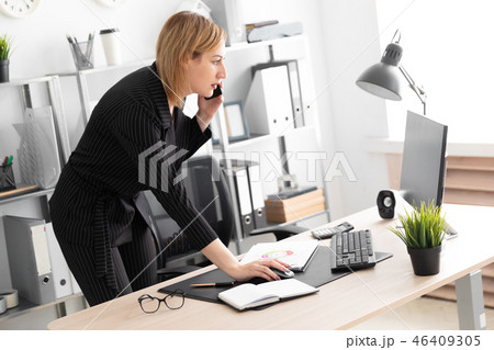 A young girl in the office talking on the phone and bent over the Desk. 46409305