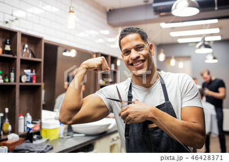 Young hispanic haidresser and hairstylist standing in barber shop, flexing muscles. 46428371