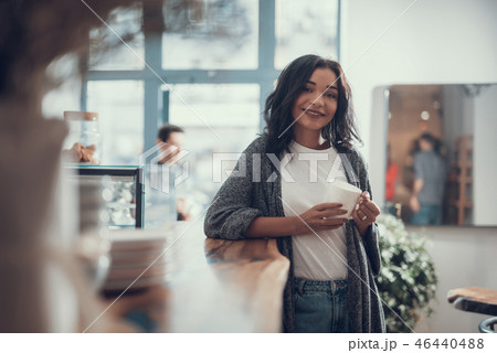 Happy lady holding white cup and standing near the bar counter 46440488