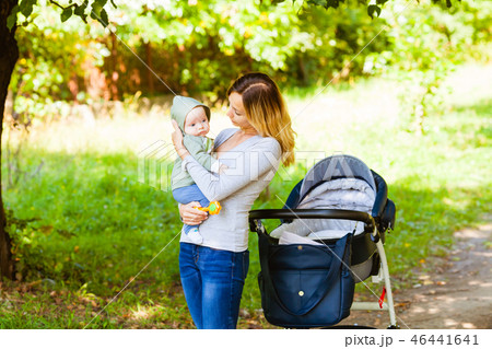 Side view of mother holding baby standing near stroller 46441641