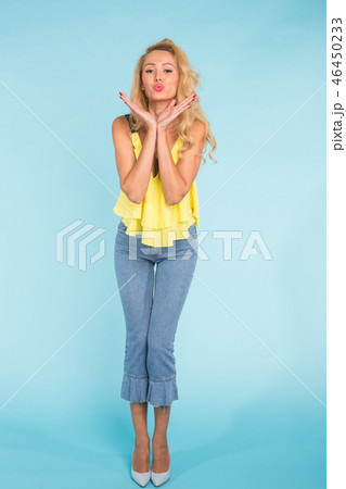 Happy caucasian blonde young woman dressed in jeans and top posing on blue background. Happy caucasian blonde young woman dressed in jeans and top posing on blue background. 46450233