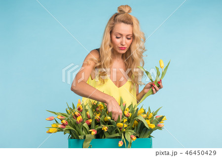 Happy beautiful blonde caucasian woman with big box of tulips on blue background. 46450429