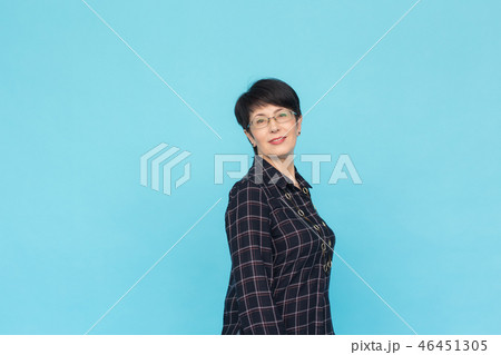 Portrait of middle-aged woman with short hair wearing glasses standing against blue background with 46451305