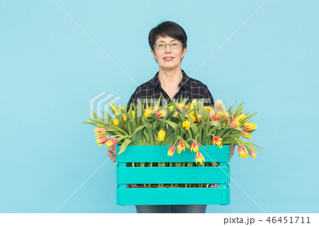 Middle-aged female florist holding blue wooden box of tulips in studio 46451711