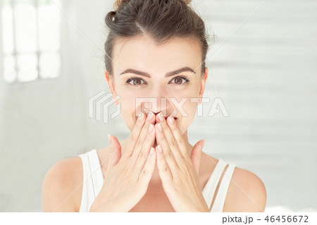 Close-up surprised happy female portrait with brown eyes holding hands on cheeks indoors at white 46456672