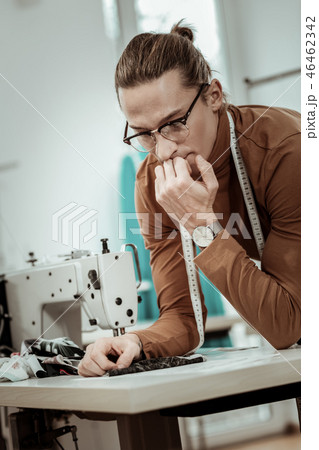 Young tall dressmaker in eyeglasses thinking about fabric for a new dress Young tall dressmaker in eyeglasses thinking about fabric for a new dress 46462342