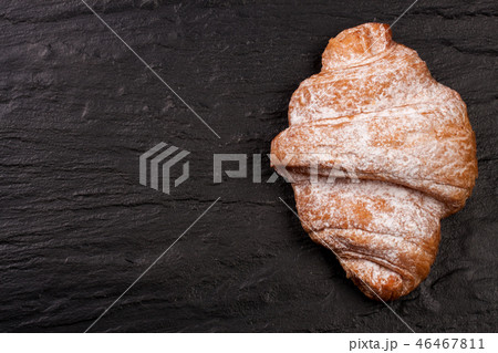 one croissant sprinkled with powdered sugar on black stone background with copy space for your text one croissant sprinkled with powdered sugar on black stone background with copy space for your text 46467811