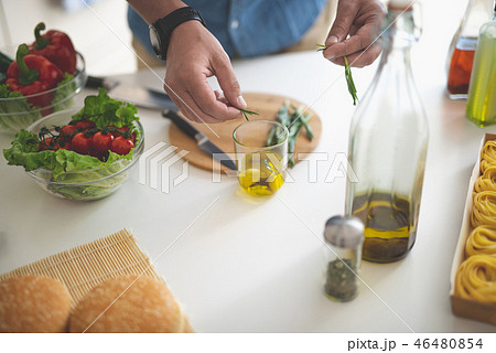 Man adding herbs to glass of olive oil Man adding herbs to glass of olive oil 46480854