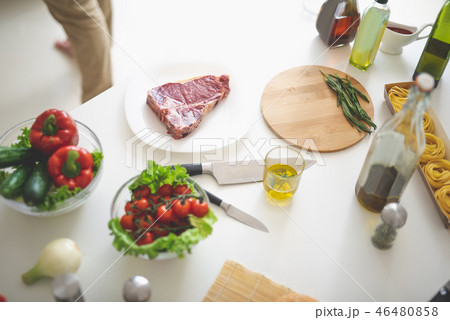 Kitchen table with meat, vegetables, olive oil, cutting board and knifes 46480858