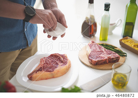 Man cooking meat while standing near white kitchen table 46480872
