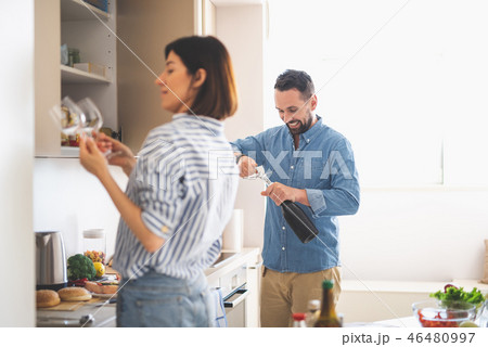 Smiling man opening bottle of wine while lady holding glasses 46480997