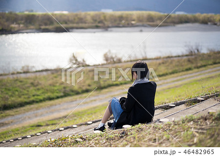 川の土手で座っている女性の写真素材