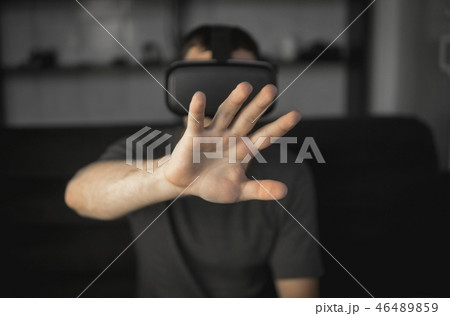 Young bearded man wearing headset of virtual reality in office sitting on a sofa and trying to touch Young bearded man wearing headset of virtual reality in office sitting on a sofa and trying to touch 46489859