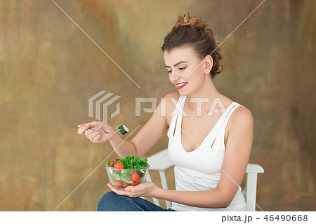 Gorgeous healthy woman sitting on a white chair eating a healthy salad from arugula, organic 46490668