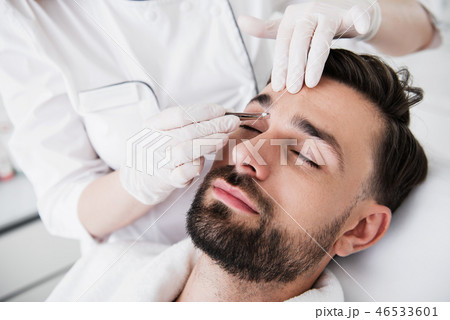 Pair of tweezers in hands of cosmetologist plucking eyebrows 46533601