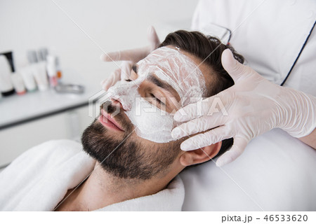 Hands in gloves touching white clay mask on the male face 46533620