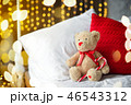 Two teddy bears siting on the bed with red candys near christmas tree. 46543312