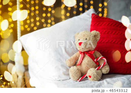 Two teddy bears siting on the bed with red candys near christmas tree. 46543312