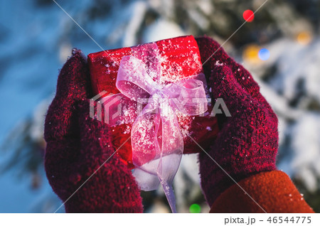 Close-up Female hands holding red Christmas gift in red mittens in the forest against the background 46544775