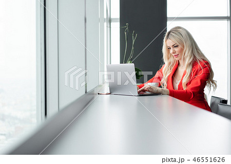 Woman in red coral business suit. Young blonde businesswoman with modern gray laptop in the office Woman in red coral business suit. Young blonde businesswoman with modern gray laptop in the office 46551626