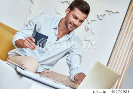 Handsome young man is sitting at travel agency with laptop and passport 46570923