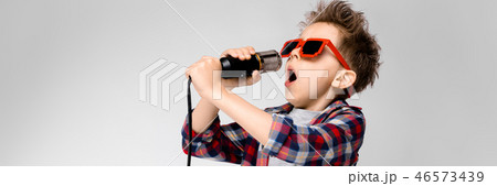 A handsome boy in a plaid shirt, gray shirt and jeans stands on a gray background. A boy wearing A handsome boy in a plaid shirt, gray shirt and jeans stands on a gray background. A boy wearing 46573439