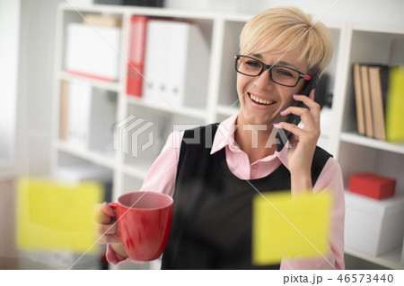 Young girl standing in the office near a transparent Board with stickers and talking on the phone Young girl standing in the office near a transparent Board with stickers and talking on the phone 46573440