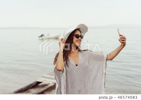Cheerful young girl in summer hat and swimwear taking a selfie Cheerful young girl in summer hat and swimwear taking a selfie 46574083