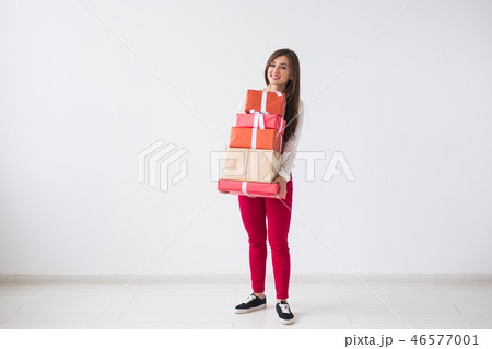 Christmas and holidays concept - young woman holding stack of gift boxes over white background with 46577001