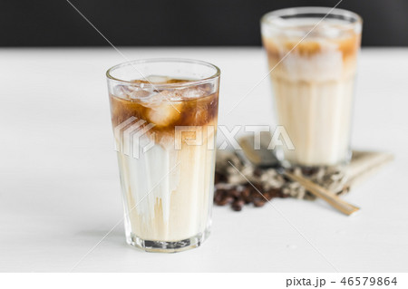 Ice coffee in a glass with cream over and coffee beans on the table Ice coffee in a glass with cream over and coffee beans on the table 46579864