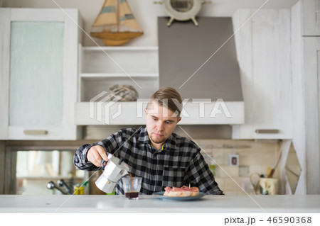 People, breakfast and drinks concept - handsome bearded young man is drinking coffee in kitchen People, breakfast and drinks concept - handsome bearded young man is drinking coffee in kitchen 46590368